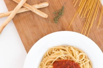 white ceramic bowl with pasta and red tomato on brown wooden table