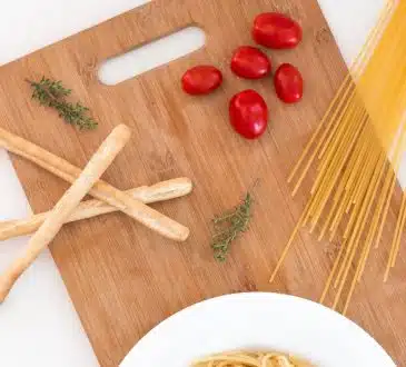 white ceramic bowl with pasta and red tomato on brown wooden table