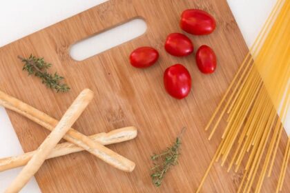 white ceramic bowl with pasta and red tomato on brown wooden table