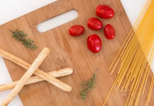 white ceramic bowl with pasta and red tomato on brown wooden table