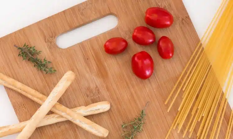 white ceramic bowl with pasta and red tomato on brown wooden table